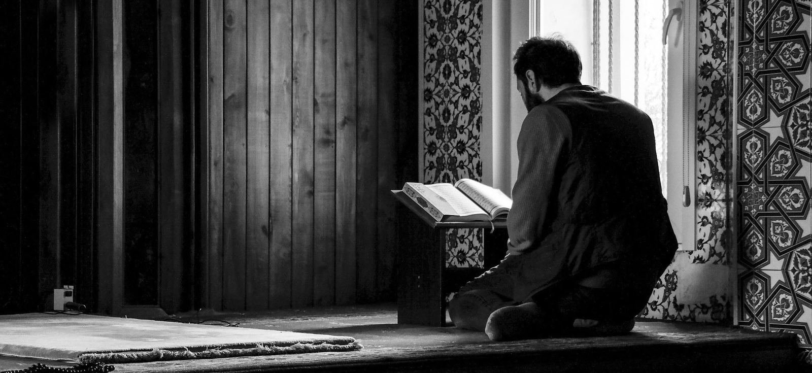 A man reciting the Qur'an from a rehal in a quiet mosque